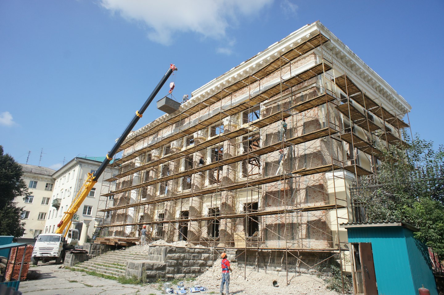Operai edili ristrutturano un edificio in mattoni con ponteggi e una gru.