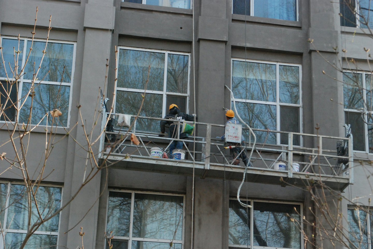 Operai edili applicano intonaco a un edificio da ponteggi sospesi.